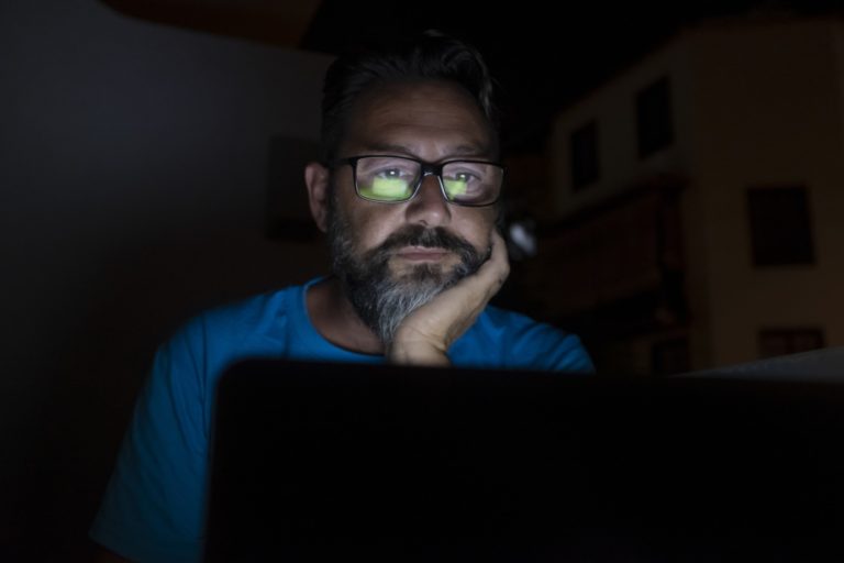 Stressed and worried man work by night on laptop computer - online social media life and stress
